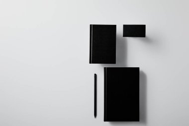 top view of arranged black notebooks with business card and pencil on white surface for mockup clipart