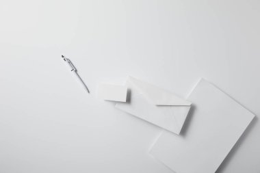 kalem, boş kağıt ve kartvizit ile düzenlenmiş zarf üstten görünüm mockup için beyaz yüzeyi