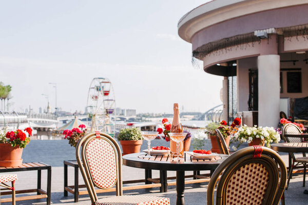 bottle of champagne, glasses and gourmet desserts on round table in outdoor cafe 