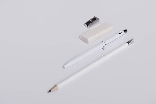 close-up shot of pen with pencil, eraser and sharpener arranged in row on white surface for mockup