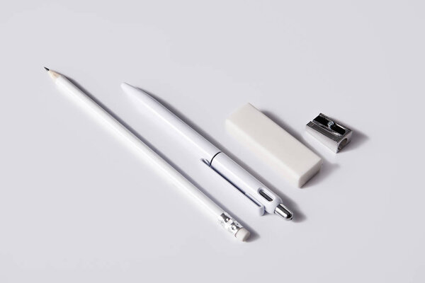 close-up shot of pen with pencil, eraser and sharpener in row on white surface for mockup