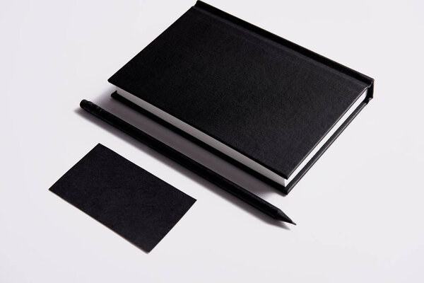isometric view of black notebook with pencil and business card on white tabletop for mockup
