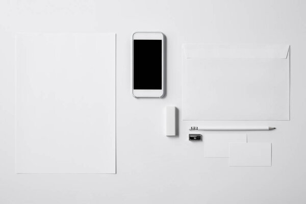 top view of smartphone with blank screen and office supplies on white tabletop for mockup