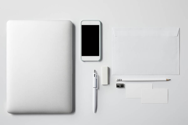 top view of laptop with smartphone and office supplies on white tabletop for mockup
