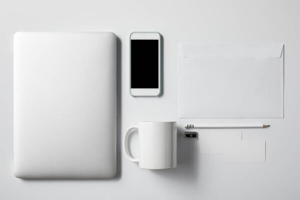 top view of laptop with smartphone, cup and office supplies on white tabletop for mockup
