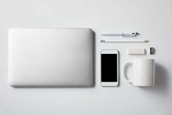 top view of laptop with smartphone and office supplies on white tabletop for mockup