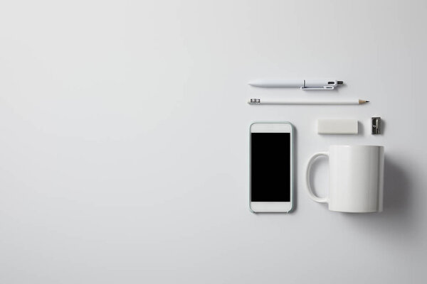 top view of smartphone with various supplies and cup on white surface for mockup