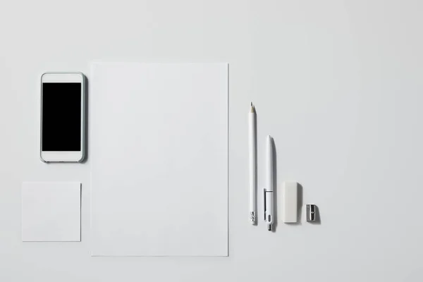 在白色桌面上为样机提供各种耗材的智能手机的顶级视图 — 图库照片