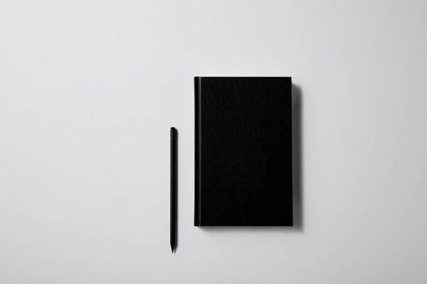 top view of black notebook with pencil on white surface for mockup