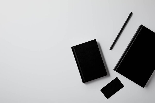 top view of black notebooks with business card and pencil on white tabletop for mockup