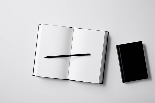 top view of black notebooks with pencil on white surface for mockup