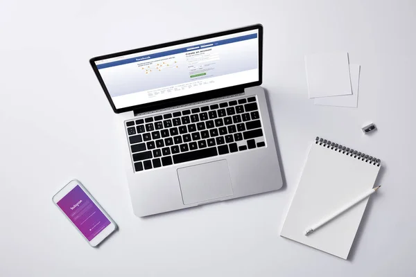 笔记本电脑与 Facebook 网站上的屏幕和智能手机与 Instagram 应用程序在白色桌面上的顶级视图 — 图库照片