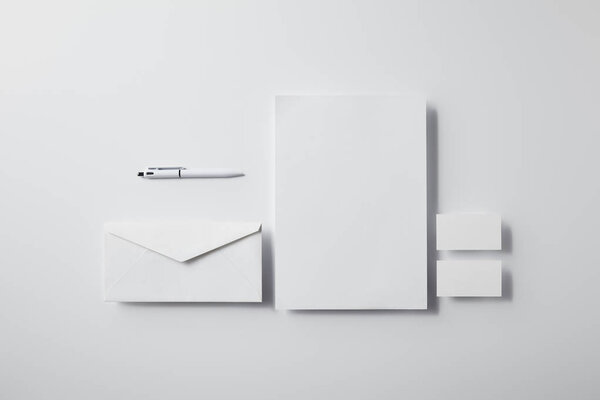 top view of layered envelope with pen, blank paper and business cards on white surface for mockup