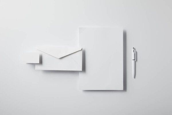 top view of layered envelope with pen, blank paper and business card on white tabletop for mockup