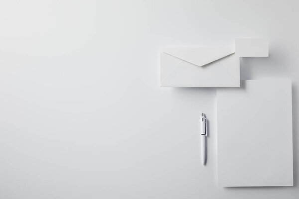 top view of layered envelope with pen, blank paper and business card on white surface for mockup
