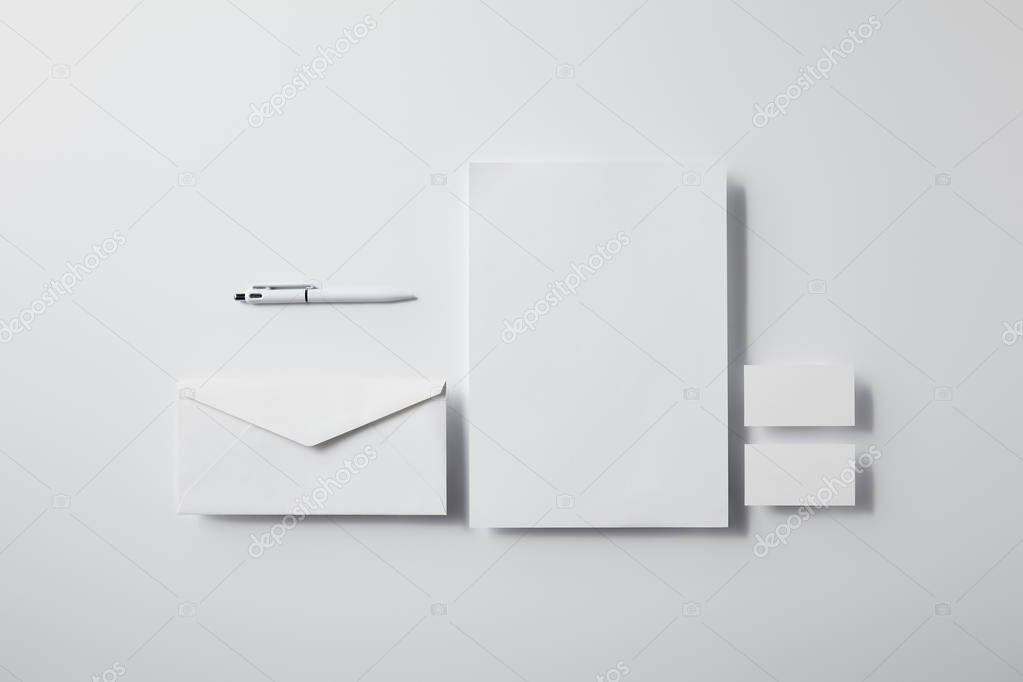 Top view of layered envelope with pen, blank paper and business cards on white surface for mockup