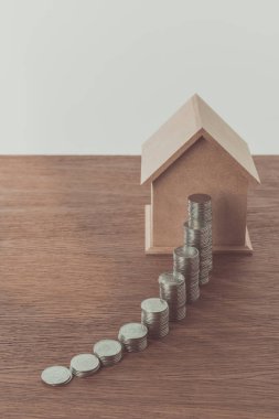 stacks of coins and small wooden house on wooden table, saving concept clipart