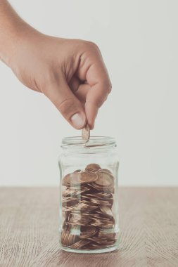 cropped image of man putting coin into glass jar on wooden table, saving concept clipart