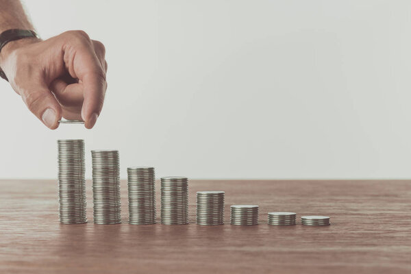 cropped image of man stacking last coin on wooden table, saving concept