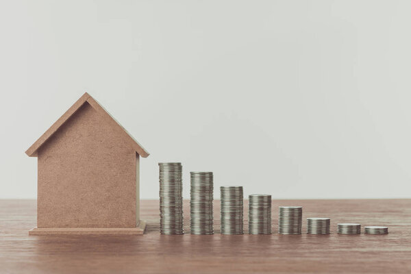 small wooden house and stacks of coins on wooden table, saving concept
