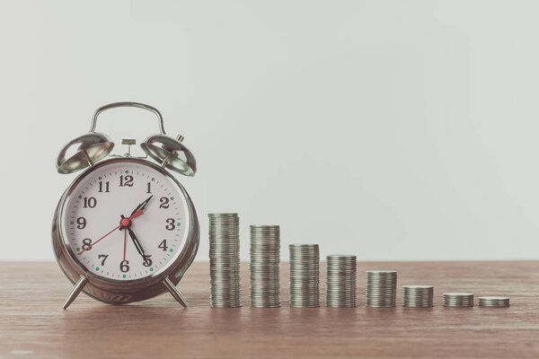 alarm clock and stacks of coins on wooden table, saving concept