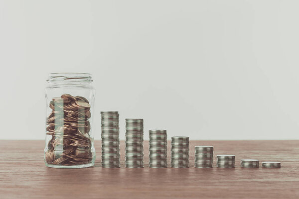 jar with coins and stacks of coins on wooden table, saving concept