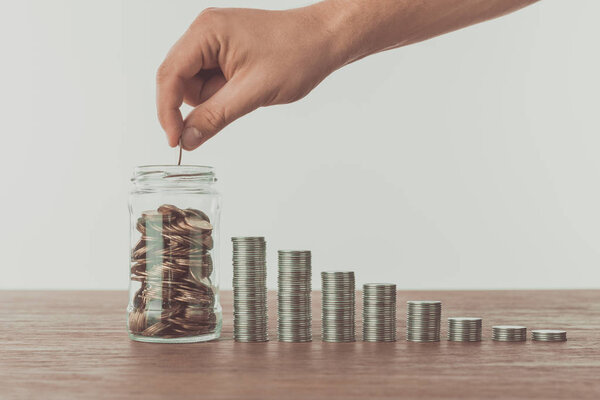 cropped image of man putting coin into jar on wooden table, saving concept