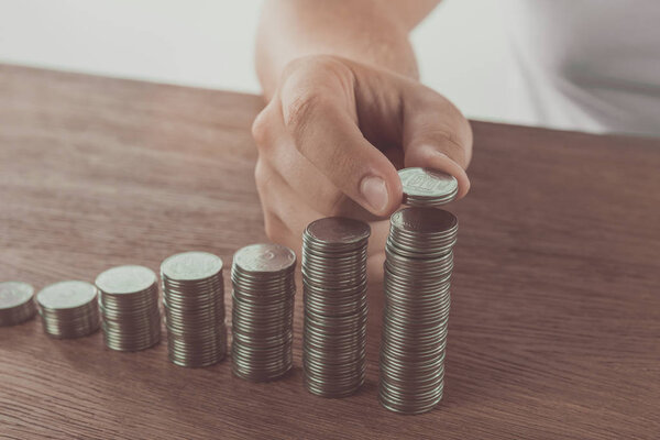 cropped image of man stacking coins on wooden table, saving concept