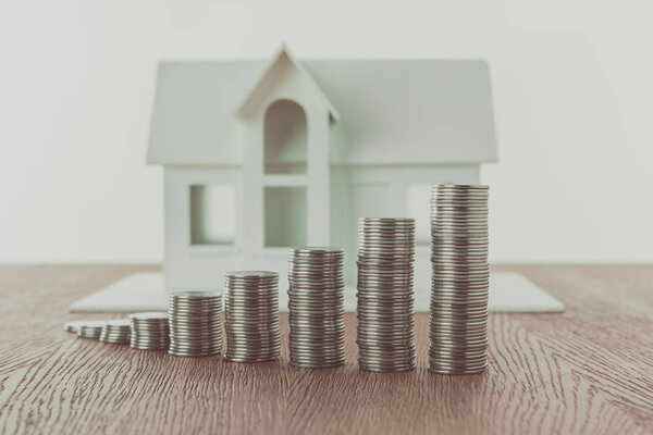 stacks of coins on wooden table in front of small wooden house, saving concept