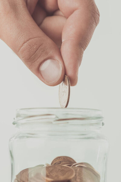 cropped image of man putting coin into glass jar isolated on white, saving concept