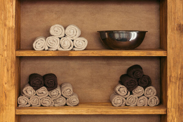 close-up view of empty metal bowl and rolled towels on wooden shelves
