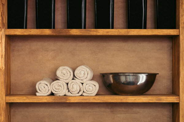 close-up view of empty metal bowl, rolled towels and glass containers on wooden shelves 