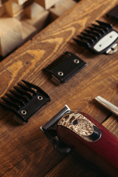 close-up view of electric clipper with various nozzles on wooden shelf in barbershop