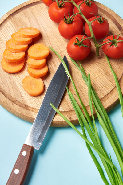 close up view of knife and assorted fresh vegetables on wooden cutting board on blue background