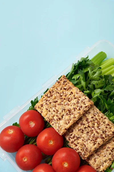 close up view of food container full of healthy vegetables and cookies isolated on blue