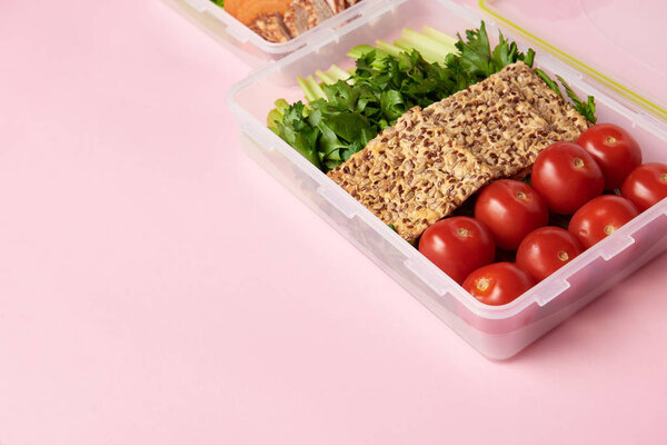 close up view of healthy food arranged in food containers on pink backdrop