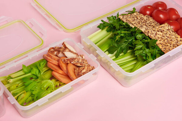 close up view of healthy vegetables and cookies arranged in food containers on pink backdrop