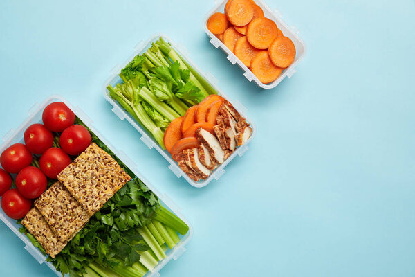 top view of arrangement of food containers with fresh healthy vegetables, meat and cookies isolated on blue