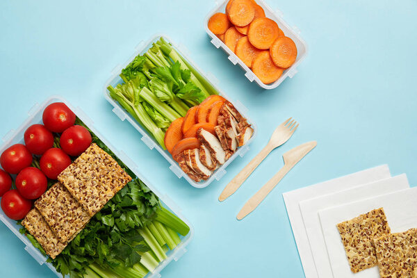 top view of arrangement of food containers with fresh healthy food and cutlery isolated on blue