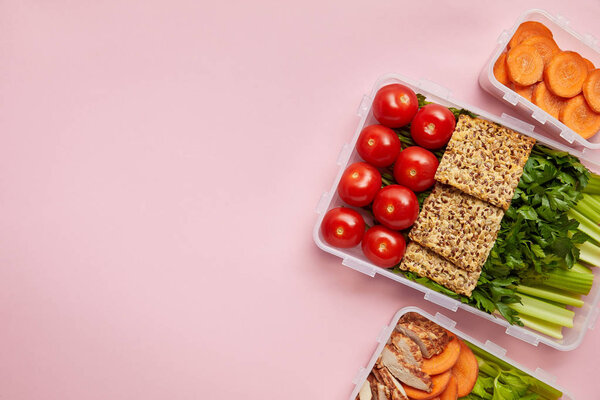 flat lay with  fresh vegetables and cookies arranged in food containers isolated on pink