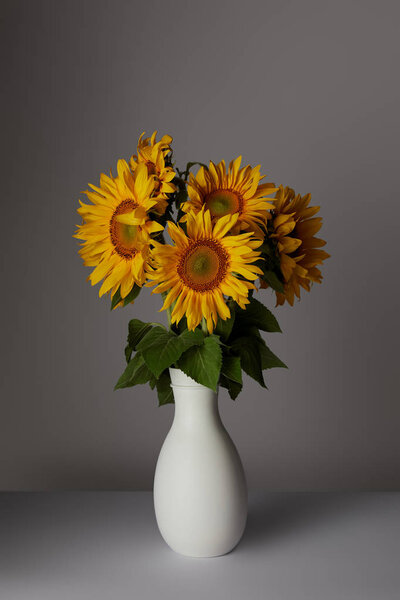 beautiful bouquet of yellow sunflowers in vase, on grey
