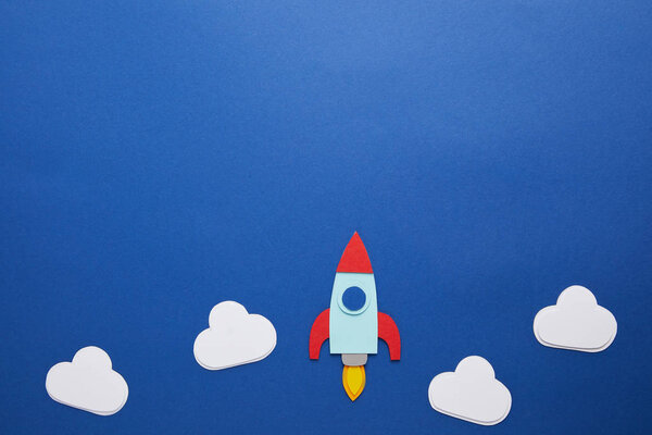 clouds and rocket on blue paper background with copy space