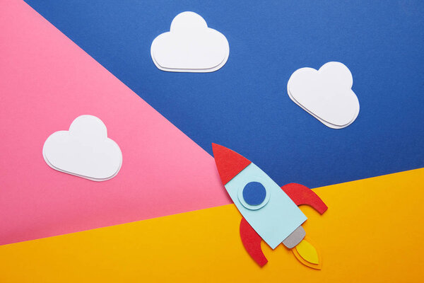 top view of clouds and colorful rocket on creative paper background
