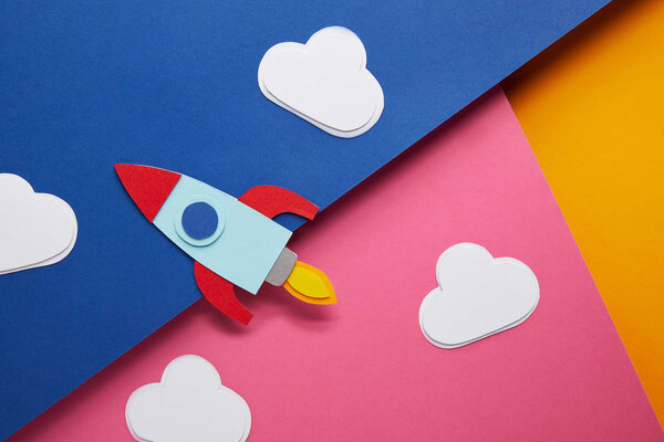 top view of clouds and rocket on colorful paper background