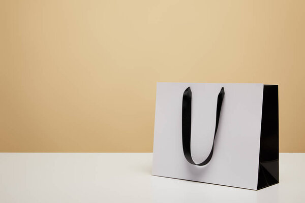 one white shopping bag with black handle on white table isolated on beige