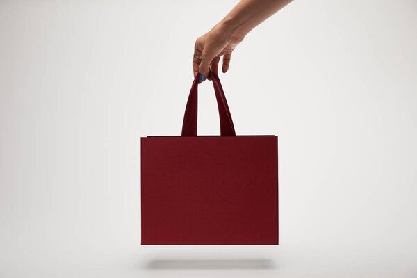 cropped image of woman holding burgundy shopping bag in hand isolated on white 