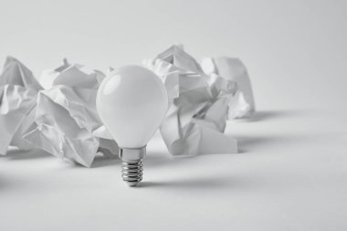 close-up shot of power saving light bulb with crumpled papers on white clipart