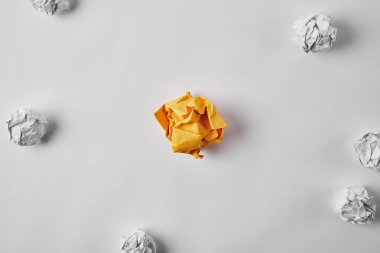 top view of crumpled yellow paper surrounded with white crumpled papers on white surface clipart