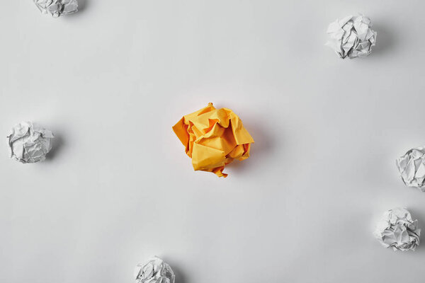top view of crumpled yellow paper surrounded with white crumpled papers on white surface