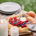Pie with berries, candles on table in garden